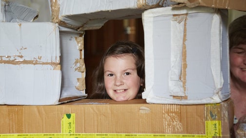A child looking out through a window within a castle made of cardboard boxes